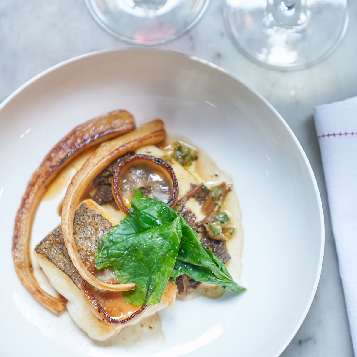 A plate of food with great presentation and two wine glasses visible.