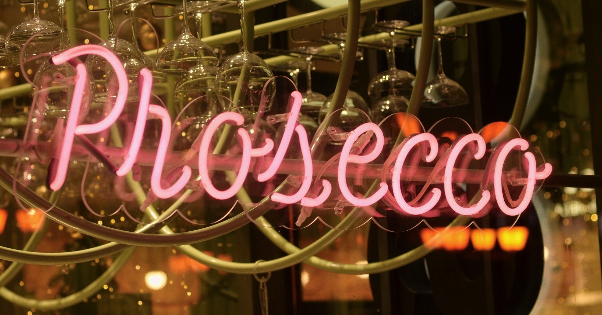 A neon pink sign reading 'Prosecco' at a bar.